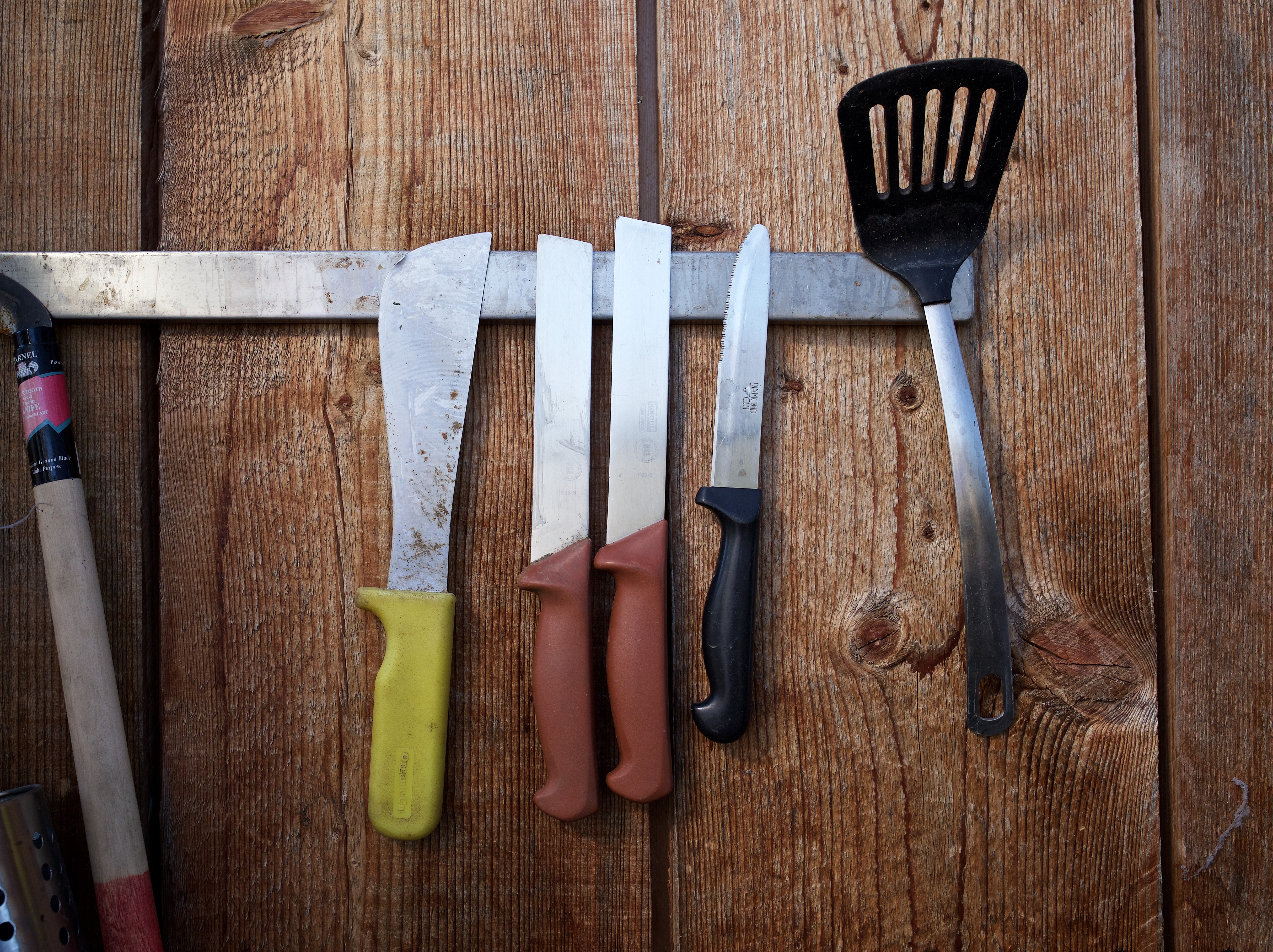 Harvest knives and other tools hanging from magnetic rack against a wood wall