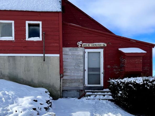 red barn with a sign that reads "Milk House" and snow on the ground