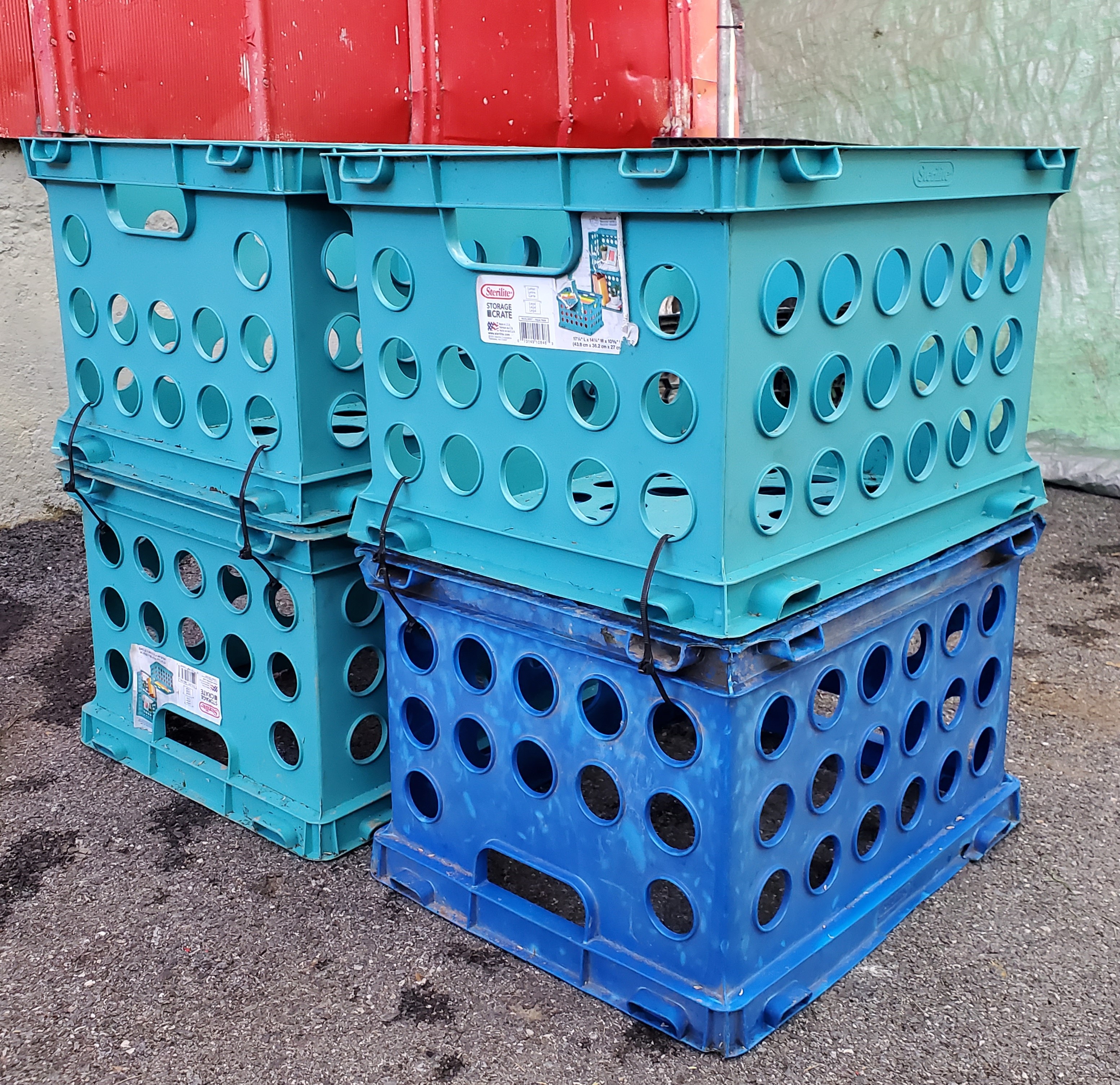 Teal and blue plastic crates stacked on an asphalt surface.