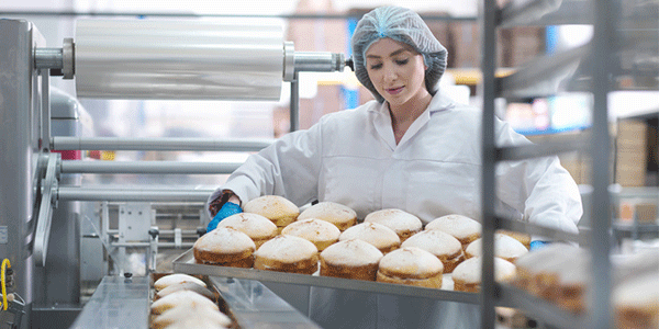 a baker in a uniform and hairnet with freshly-baked cakes