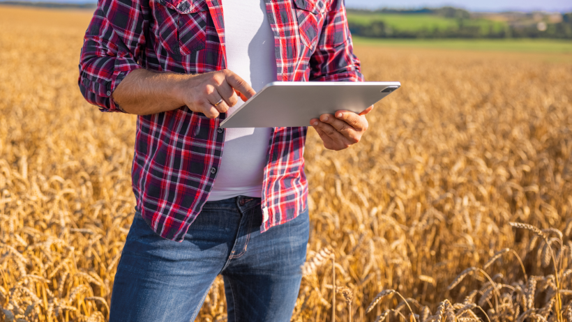 A person wearing jeans and a red checkered flannel stands in a field looking at a tablet.