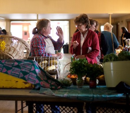 A farmer and customer discussing products in an indoor market.