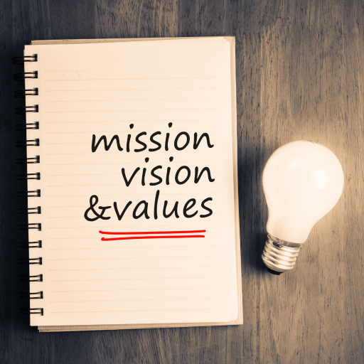 A notebook with the words "mission, vision, and values" and a lightbulb on a flat surface.