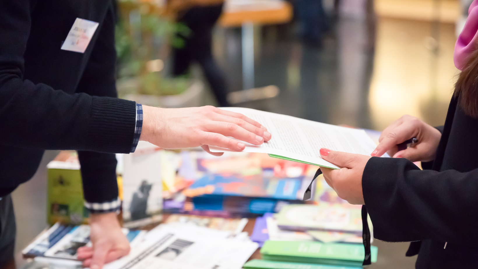 two people are standing over a table with a bunch of marketing materials on it discussing something on a piece of paper