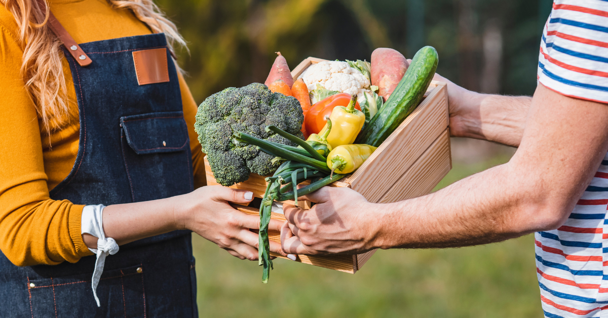 A farmer hands a box of vegetables to a customer