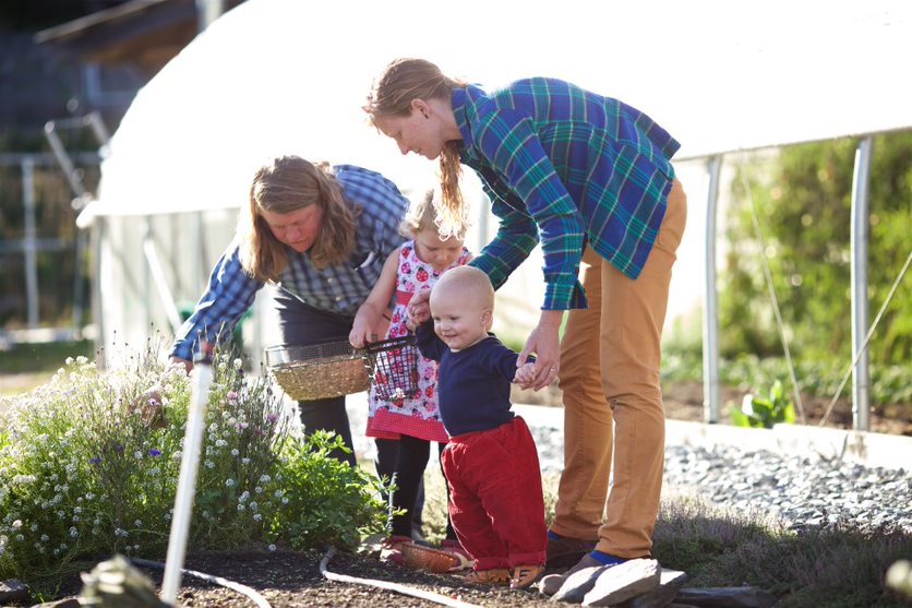 A farmer demonstrating to a mom and two children how to harvest flowers.