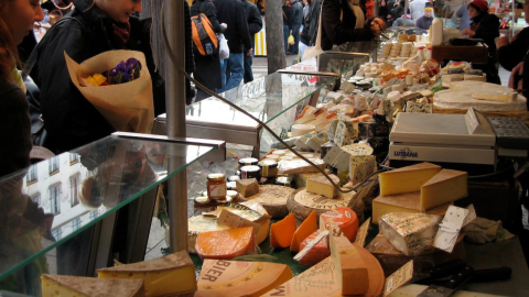 Various cuts of cheese at outdoor market as people look on from left