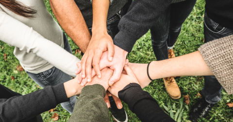 A group of people standing over grass with their hands touching in the middle