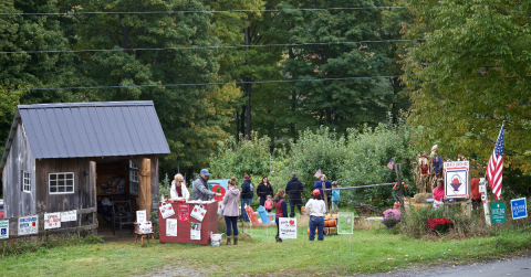 A crowd stands outside of a farm stand offering pick your own apples