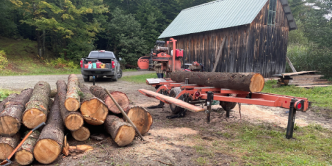 A pile of timber with a truck and a barn in the background