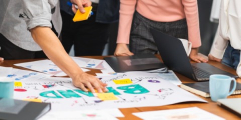 a close-up image of people pointing to a white paper with brand in large green letters