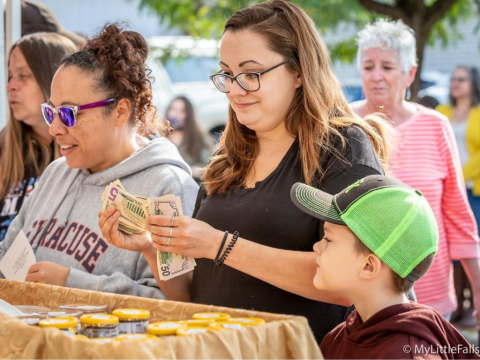 A photo of people purchasing specialty food products in jars at an outdoor vendor booth.