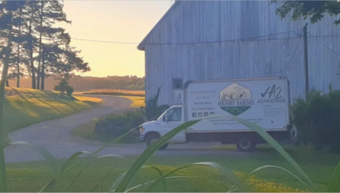 Henry Farms box truck on gravel driveway in front of barn with grass and trees 