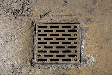A photo of a square drain covered with a metal grate set in a concrete floor.