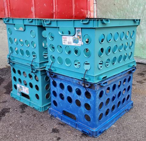 Teal and blue plastic crates stacked on an asphalt surface.