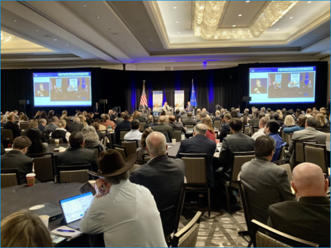 conference attendees sit at round tables and listen to keynote speaker