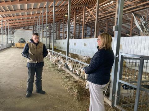 USDA Under Secretary Jenny Lester Moffitt chatting with Miles Hooper of Ayers Brook Goat Dairy in Randolph, VT in a barn next to a pen with goats.