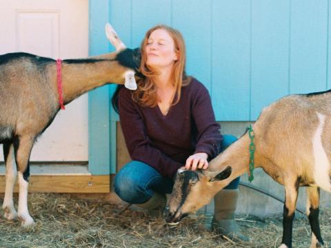 dairy farmer kneeling with two of her goats