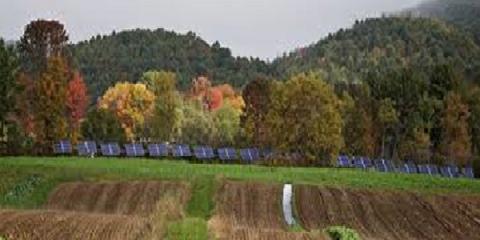 solar panels behind a tilled field with trees and mountains in the background