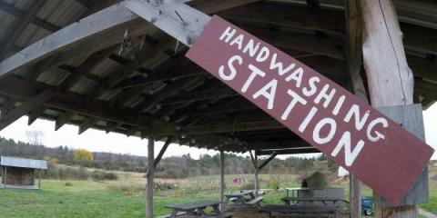 A red sign with white text that reads "Handwashing Station" on a wood open-air produce wash/pack area