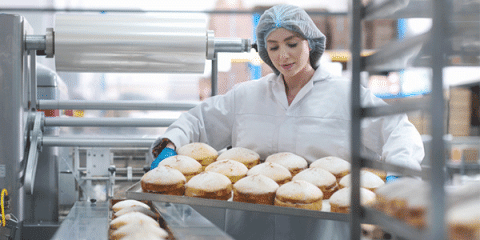 a baker in a uniform and hairnet with freshly-baked cakes